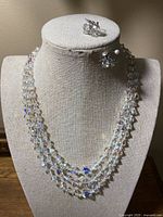Front view of multi-strand crystal bead necklace draped on display bust with matching earrings pinned above.