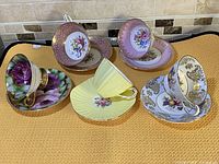 Set of 5 fine bone china cups and saucers displayed on yellow cloth with various floral and solid colored patterns.
