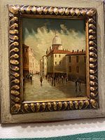 Full view of the framed oil painting showing cityscape with pedestrians and domed building, highlighting the frame and signature.