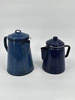 Two blue tin pitchers, one tall and one short, both with lids and handles, placed side by side on a white background.
