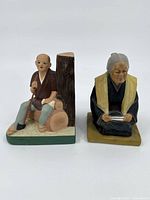 Ceramic statues of elderly Asian man and woman, front view on plain background.
