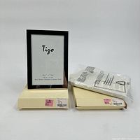 Photo showing two silver plated Tigo picture frames, each with a 4x6 inch opening, one positioned upright on its box and the other box closed with protective packaging.