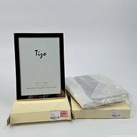 Two silver plated Tigo picture frames shown with original beige boxes and protective plastic covering.