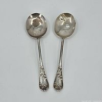 Two sterling silver spoons with floral pattern on handles, bowls facing upward.