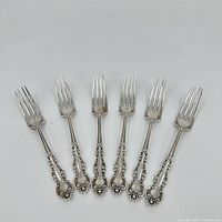 Six forks laid flat against white background showing ornate handles and four-tine fork ends
