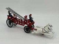 Full view of cast iron fire truck carriage with two white horses and two firefighter figurines.