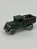 Side view of a small green cast iron truck figurine with open cargo bed, showing details of cab and wheels.