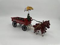 Full view of the cast iron Schultz Beer & Ale decorative wagon pulled by two brown horses with driver under umbrella.