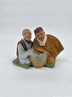 Front view of the ceramic statue showing both elderly figures with detailed faces and clothing next to a ceramic pot.