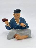 Front view of ceramic statue showing Asian man seated cross-legged with hammer and chisel.