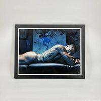 Front view of framed portrait art print showing tattooed man lying prone on leather surface with blue background.