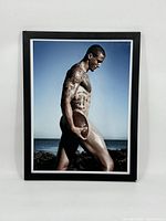 Framed color photographic portrait of Colin Kapernick holding football, profile view on beach.