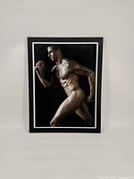 Front view of a framed photographic portrait showing a nude male, Colin Kapernick, holding a football in profile pose.
