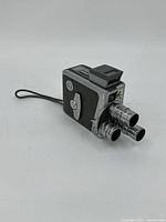 Front and side view of the Keystone K-48 Bel Air camera showing three turret lenses, textured black body, chromed metal parts, and top viewfinder.
