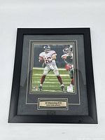 Front view of framed Eli Manning photo showing his action pose in NY Giants uniform with plaque below.