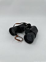 Black Official brand 8x50 binoculars on white background showing full item with leather strap and textured surfaces.