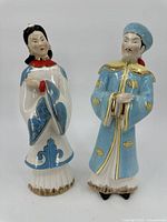 Front view of the pair of Asian man and woman porcelain statues showing intricate painted details and traditional clothing.