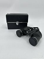 Skyline 7x35 binoculars placed next to their black carrying case showing the case locked with metal latch.