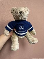 Front view of the teddy bear wearing navy blue Mercedes-Benz sweater with logo and text visible