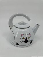 Front view of the white ceramic tea pot kettle with cat face design on the body, curved handle, and spout.