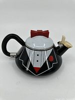 Front and side view of the tin tea kettle with tuxedo design, red bowtie lid, and cream spout cover.