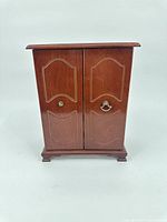 Front view of closed wooden jewelry box showing double doors and decorative panels.