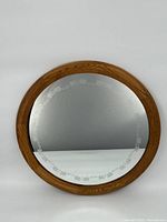Full view of circular wooden framed mirror with floral etched design on the glass's inner border.