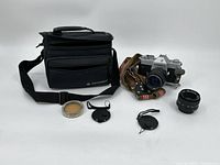 Full lot photo showing the Yashica TL Electro-X camera with attached lens, additional lens, striped camera strap, lens filters, lens caps, and the black carrying bag.
