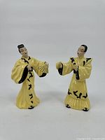 Front view of yellow dressed Asian man and woman ceramic statues; the woman has a broken head.