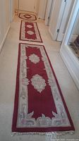 Photo showing three red floral area rug runners laid out in a hallway, highlighting their length, floral patterned medallions, and beige borders with fringe.