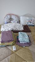 Overview of all items in the bedding lot showing nursing pillow, silk comforter, heated blanket, and folded linens.