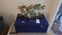 Carved jade tree displayed on a dark wooden base, placed on top of a blue case box.
