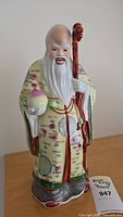 Full view of the porcelain figure showing robe details, peach, staff, and facial features.