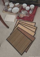 Photo showing entire dishware set with various bowls, spoons, and small plates arranged with placemats and napkin on carpeted floor.