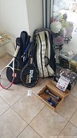 Two tennis rackets with Wilson logo and covers, fitness dumbbells and bands on floor with tennis bag.