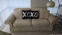 Front view of beige patterned Flexsteel sofa with three decorative pillows including black XOXO pillow.