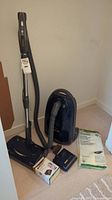 Full view of Kenmore vacuum cleaner with hose, wand, brush attachments, and vacuum bags on carpeted floor.