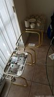 Three gold-tone metal frame nesting tables with glass tops arranged from smallest to largest. The smallest table is shown with some wobble. Silverware and cups on the largest table are not included.