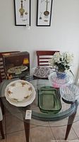 Glass table with variety of serving dishes, ceramic vase, and tablecloth visible