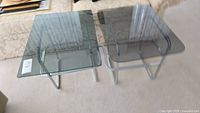 Two vintage chrome-framed tables with tinted glass tops, showing difference in shape and size.