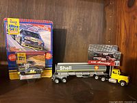 Lot of three die cast vehicles including the Sunoco Ultra 94 race car in blister pack, Mobil 1 NASCAR car in boxed packaging, and Shell Oil tanker truck with yellow cab on display shelf.