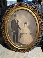 Front view of antique oval portrait photograph of a formal couple in an ornate carved wooden frame placed upright.