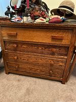 Front view of an antique tiger oak chest of drawers with four drawers. Top drawer has two rectangular wooden handles, lower drawers have round wooden knobs. Various objects are placed on top of the chest.
