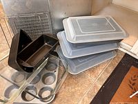 Overview of baking pans, racks, and trays stacked on tile floor showing different pan shapes and covers