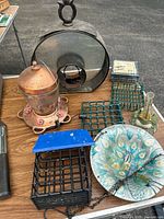 Overview of bird feeders and suet feeders on table displaying varied styles and materials including copper, glass, plastic, ceramic and metal wire cages.