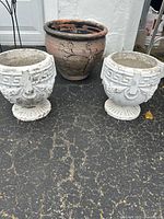 Photo showing the two white cement planters and the brown clay pottery planter arranged together on pavement with pen for size reference.