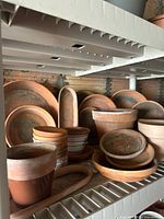 Shelf with various sizes of terra cotta clay pots, saucers, and trays showing dirt and wear.