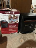 Photo of the EdenPURE electric space heater next to its original box, showing the heater's black housing and digital control panel.