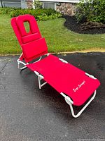 Red ergonomic lounger lawn rehab chair fully set up outdoors on blacktop with grass background, showing the lounger in a semi-reclined position.