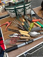 Wide view of garden hand tools and tote on table showing various hand tools including shears, trowels, and rakes.